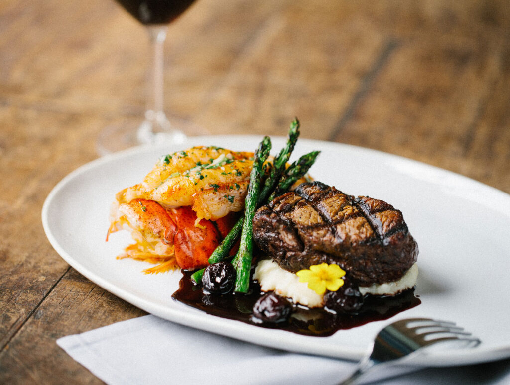 photo of a steak and seafood dinner with a glass of wine